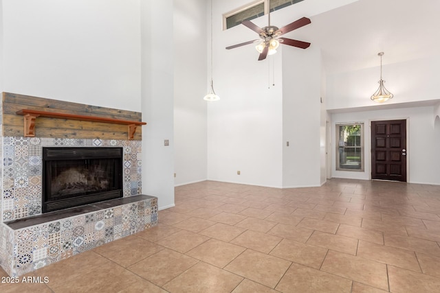 unfurnished living room featuring light tile patterned flooring, ceiling fan, a fireplace, and a high ceiling