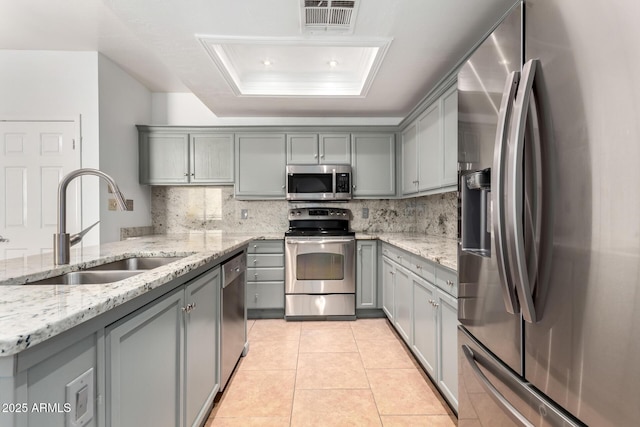 kitchen with a raised ceiling, appliances with stainless steel finishes, sink, and gray cabinetry