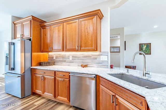 kitchen featuring sink, stainless steel appliances, light hardwood / wood-style floors, light stone countertops, and decorative backsplash