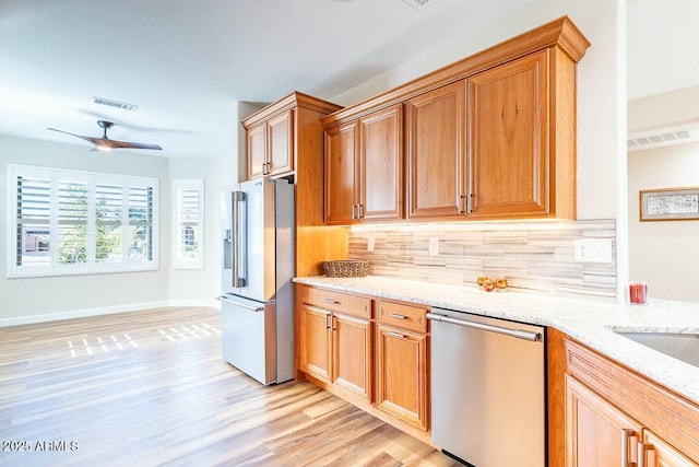 kitchen with ceiling fan, appliances with stainless steel finishes, light stone counters, tasteful backsplash, and light hardwood / wood-style floors