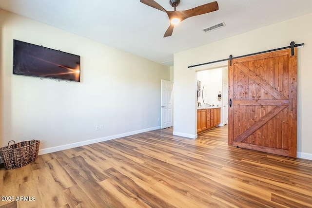 unfurnished bedroom featuring a barn door, ceiling fan, connected bathroom, and light hardwood / wood-style flooring