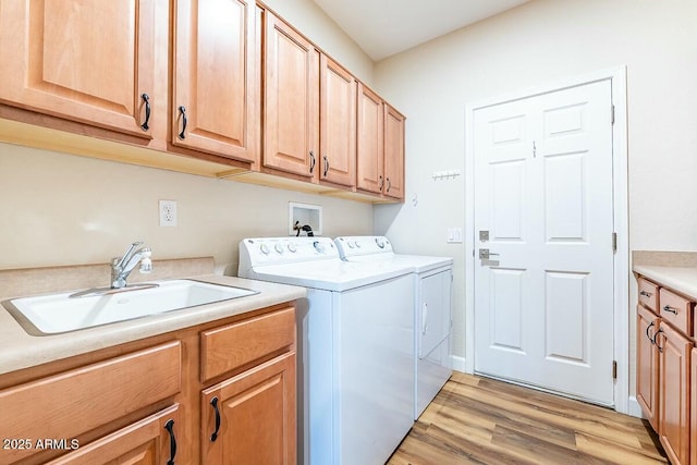 clothes washing area with cabinets, washer and dryer, sink, and light hardwood / wood-style floors