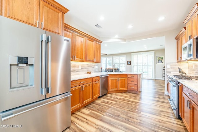 kitchen with sink, high end appliances, kitchen peninsula, light stone countertops, and decorative backsplash