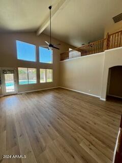 unfurnished living room featuring beamed ceiling, ceiling fan, hardwood / wood-style floors, and high vaulted ceiling