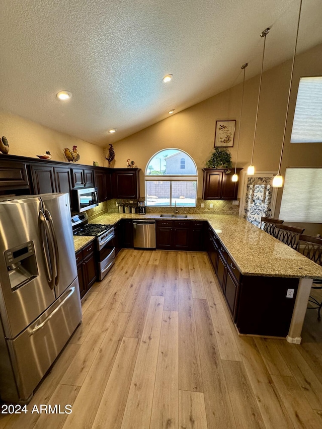 kitchen with appliances with stainless steel finishes, sink, pendant lighting, light hardwood / wood-style floors, and lofted ceiling