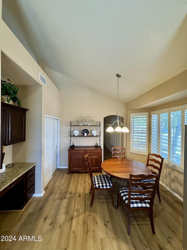 dining room with a textured ceiling, light hardwood / wood-style floors, vaulted ceiling, and an inviting chandelier