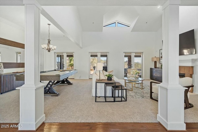 carpeted living room with billiards, a chandelier, high vaulted ceiling, and decorative columns