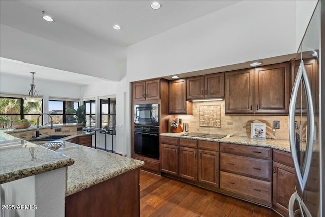 kitchen with hanging light fixtures, black appliances, sink, and light stone countertops