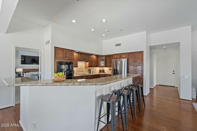 kitchen with a large island, a breakfast bar area, a towering ceiling, light stone countertops, and black appliances