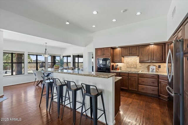 kitchen featuring tasteful backsplash, a kitchen bar, hanging light fixtures, a large island, and black appliances