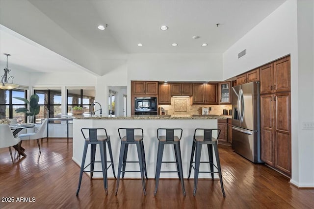 kitchen featuring stainless steel fridge, decorative light fixtures, an island with sink, and black microwave