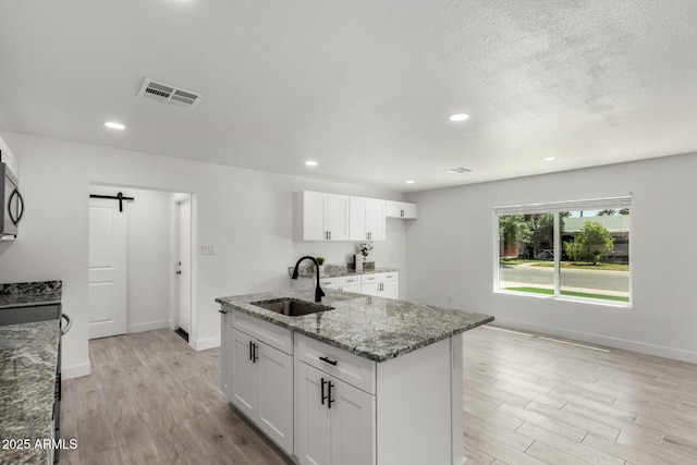 kitchen featuring light stone countertops, light wood-type flooring, visible vents, a barn door, and a sink