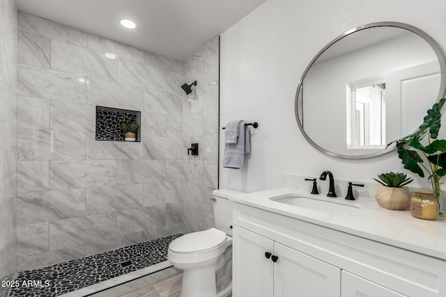 full bathroom featuring toilet, tiled shower, vanity, and recessed lighting
