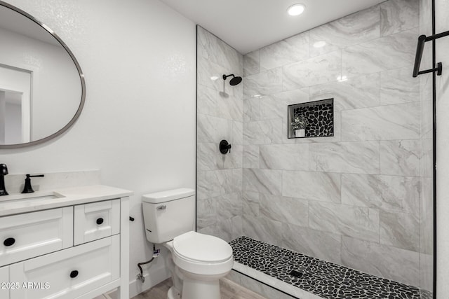 bathroom with recessed lighting, vanity, a tile shower, and toilet