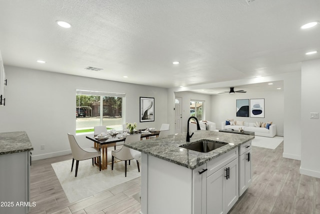 kitchen with light wood-type flooring, visible vents, stone countertops, and a sink