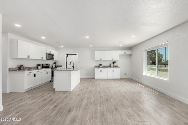 kitchen featuring baseboards, a sink, white cabinetry, light wood finished floors, and stainless steel appliances