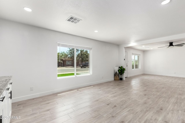 unfurnished living room with light wood-style floors, a healthy amount of sunlight, a ceiling fan, and visible vents