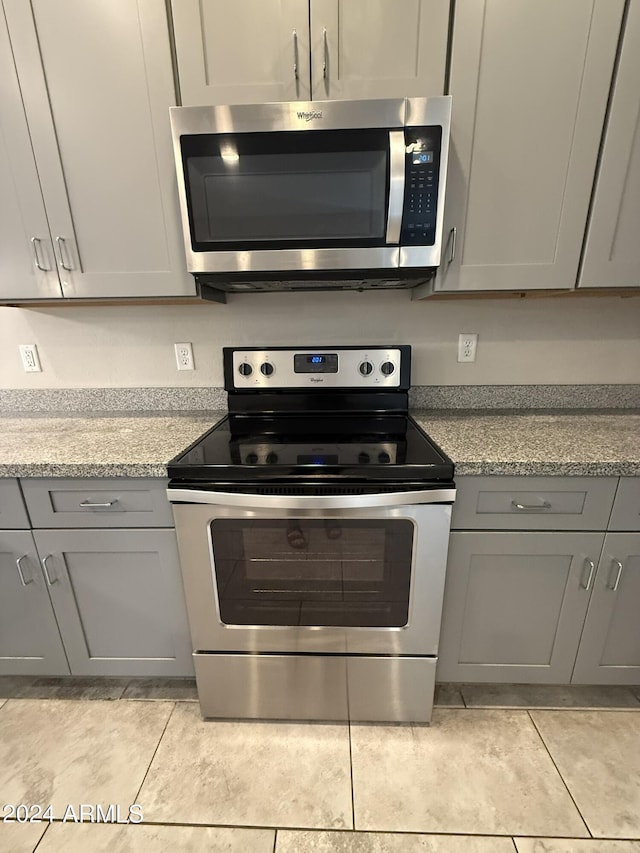 kitchen featuring gray cabinets, light stone countertops, stainless steel appliances, and light tile patterned floors