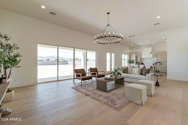 living room with a notable chandelier, a towering ceiling, light hardwood / wood-style flooring, and a healthy amount of sunlight