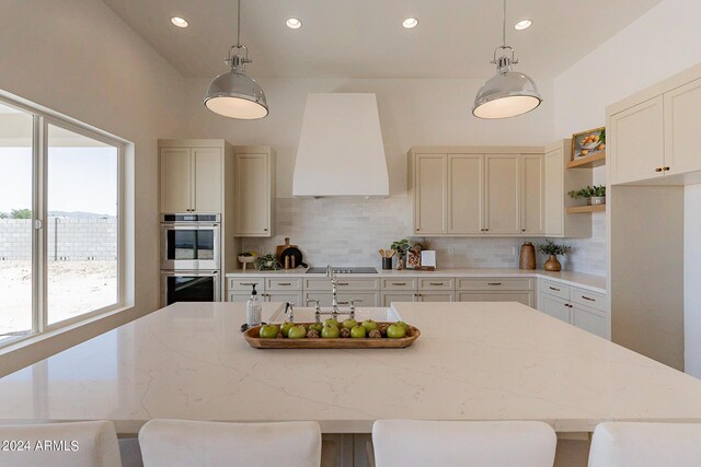 kitchen featuring decorative backsplash, stainless steel double oven, extractor fan, light stone counters, and a kitchen breakfast bar