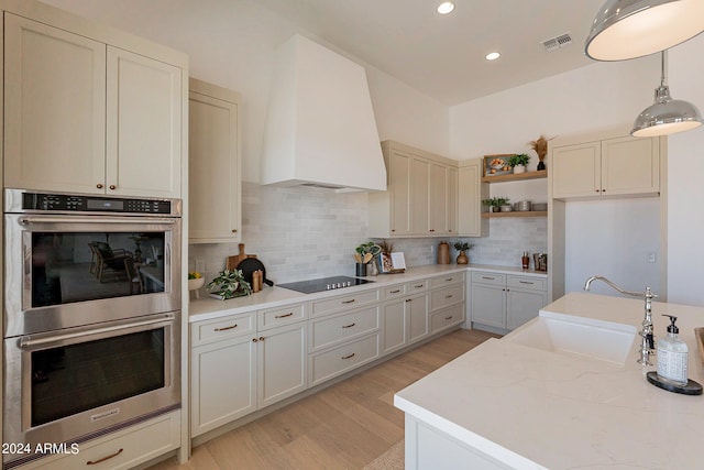 kitchen with double oven, light hardwood / wood-style flooring, decorative backsplash, custom range hood, and decorative light fixtures