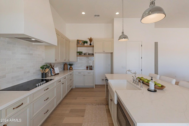 kitchen with decorative light fixtures, custom exhaust hood, a kitchen island with sink, light stone counters, and black electric cooktop