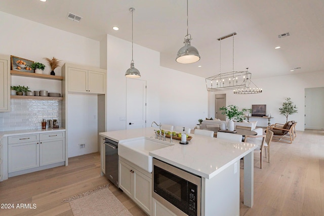 kitchen featuring black microwave, sink, hanging light fixtures, a kitchen island with sink, and stainless steel dishwasher