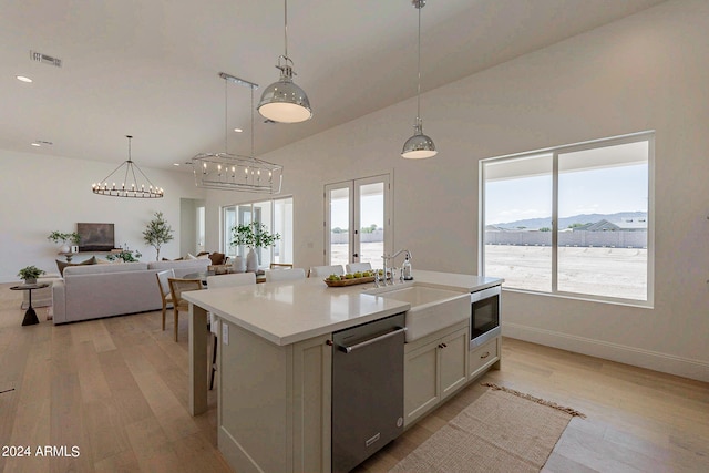 kitchen with light hardwood / wood-style floors, decorative light fixtures, an island with sink, stainless steel appliances, and sink