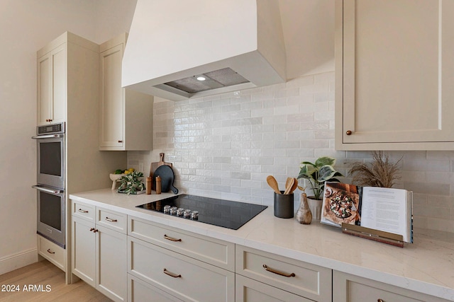 kitchen featuring decorative backsplash, custom exhaust hood, light hardwood / wood-style flooring, double oven, and black electric stovetop