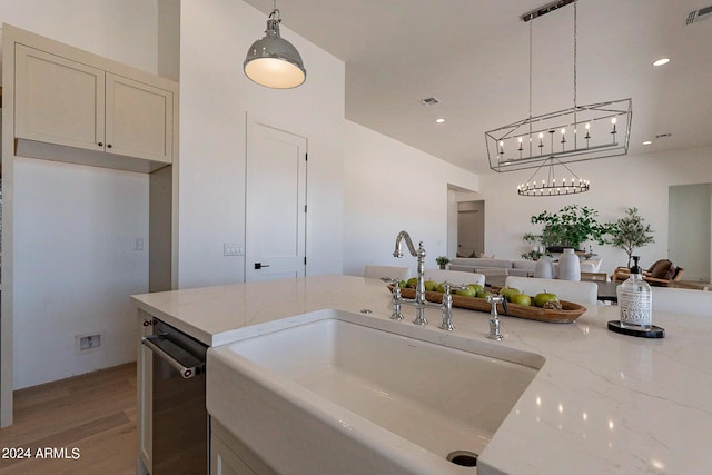 kitchen with light wood-type flooring, pendant lighting, stainless steel dishwasher, light stone countertops, and sink