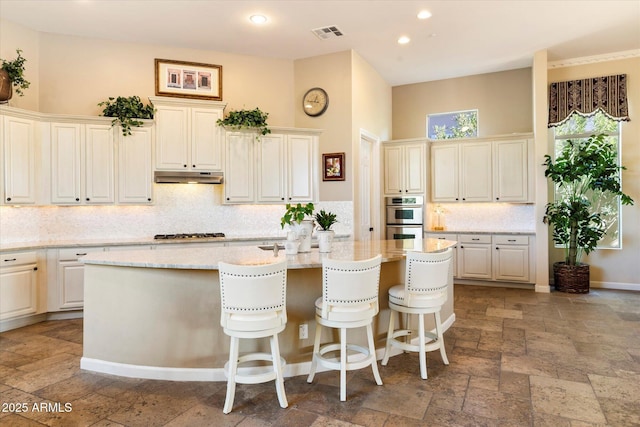 kitchen with a high ceiling, light stone counters, a kitchen bar, an island with sink, and stainless steel appliances