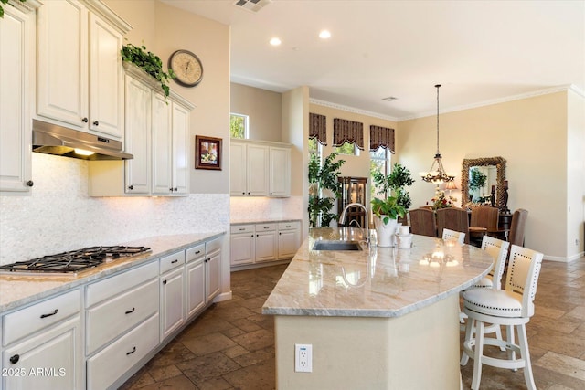 kitchen with stainless steel gas stovetop, hanging light fixtures, sink, light stone countertops, and a kitchen island with sink