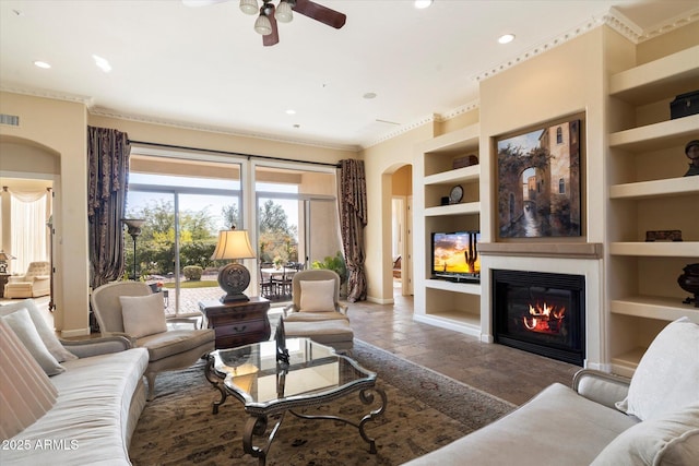 living room with built in shelves, ceiling fan, and crown molding