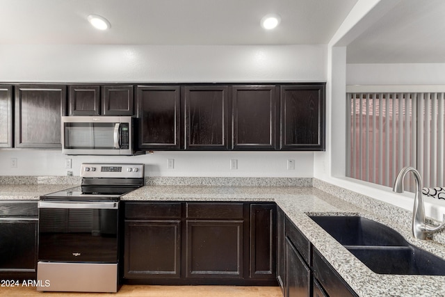 kitchen with appliances with stainless steel finishes, light stone counters, dark brown cabinets, and sink