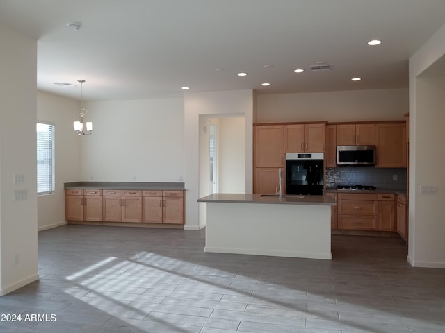 kitchen featuring backsplash, a kitchen island with sink, black appliances, hanging light fixtures, and a notable chandelier