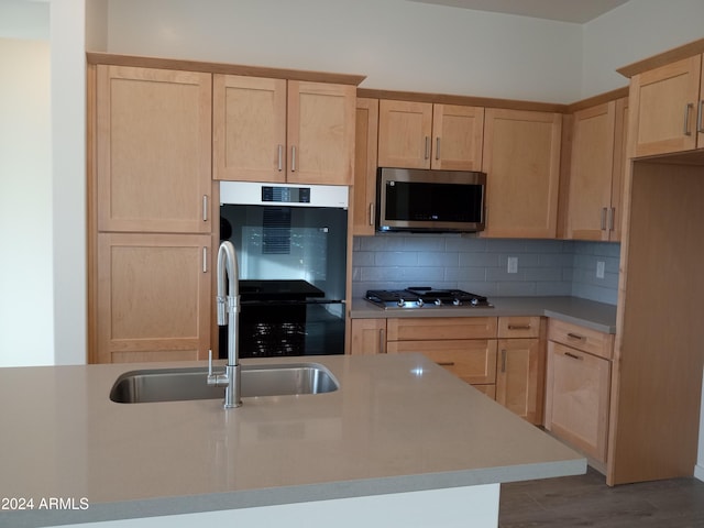 kitchen with sink, backsplash, light brown cabinetry, appliances with stainless steel finishes, and hardwood / wood-style flooring