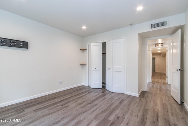 unfurnished bedroom featuring visible vents, baseboards, a closet, and wood finished floors