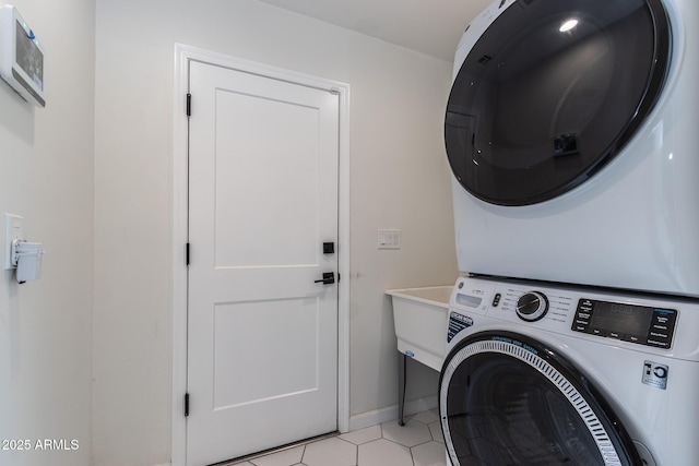 washroom featuring light tile patterned floors, baseboards, stacked washer and dryer, and laundry area