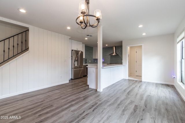 kitchen with a peninsula, stainless steel appliances, light countertops, wall chimney exhaust hood, and a chandelier