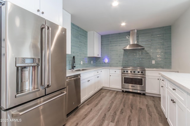 kitchen with a sink, light countertops, appliances with stainless steel finishes, wall chimney exhaust hood, and backsplash