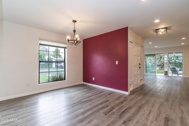 spare room featuring a notable chandelier, wood finished floors, plenty of natural light, and baseboards