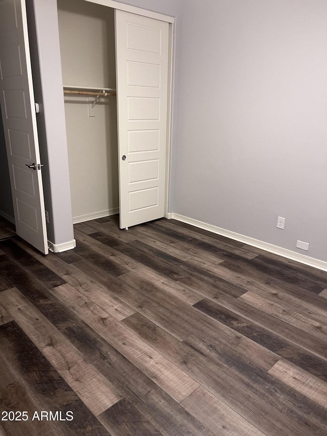 unfurnished bedroom with a closet, dark wood finished floors, and baseboards