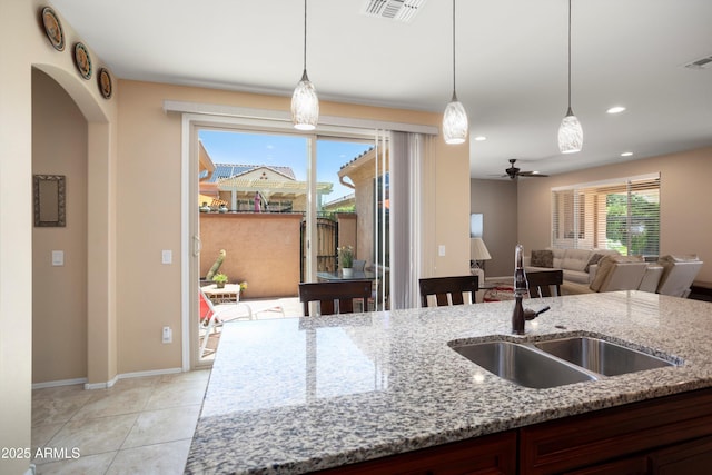 kitchen featuring visible vents, pendant lighting, light stone countertops, a sink, and open floor plan