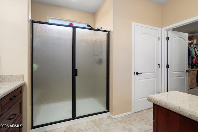 full bathroom with vanity, baseboards, tile patterned floors, a spacious closet, and a stall shower