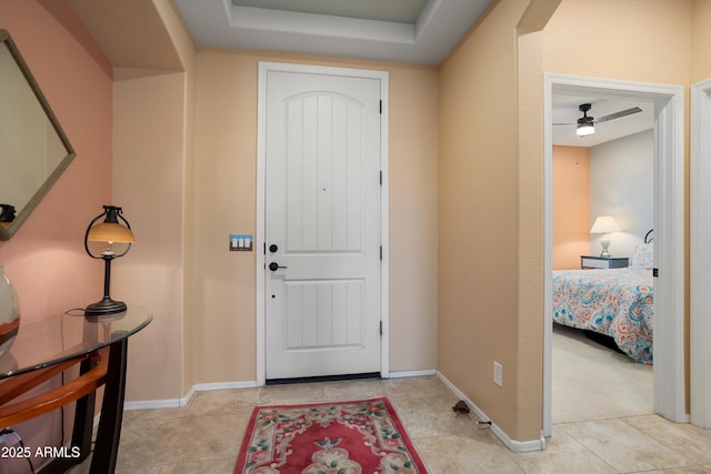 foyer with a tray ceiling, baseboards, and a ceiling fan