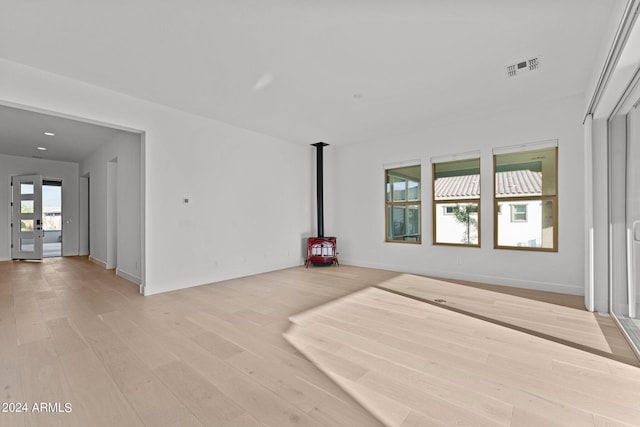 unfurnished living room featuring light wood-type flooring, a wealth of natural light, and a wood stove