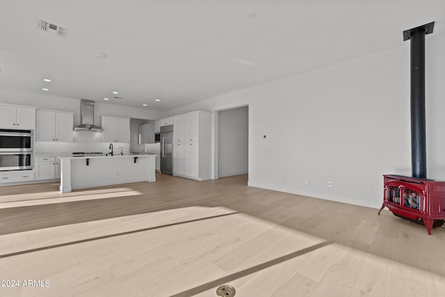 unfurnished living room with sink, light wood-type flooring, and a wood stove