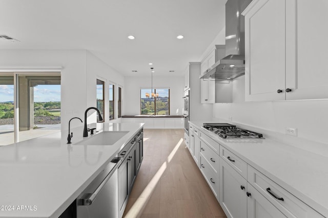 kitchen with wall chimney exhaust hood, white cabinetry, appliances with stainless steel finishes, and sink