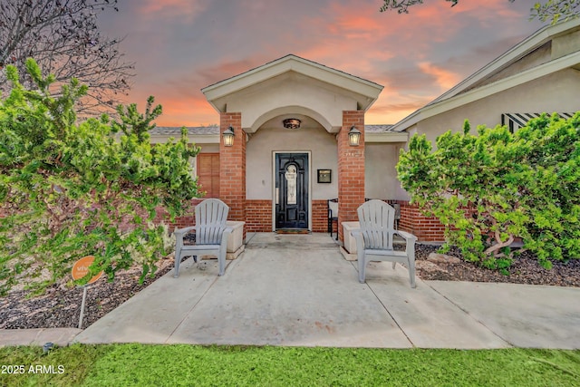 5621 N 13th St, Phoenix, AZ 85014 - doorway to property featuring stucco siding, brick siding, a patio, and a shingled roof