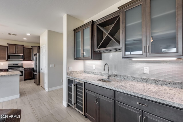 kitchen with sink, beverage cooler, light stone counters, dark brown cabinets, and appliances with stainless steel finishes